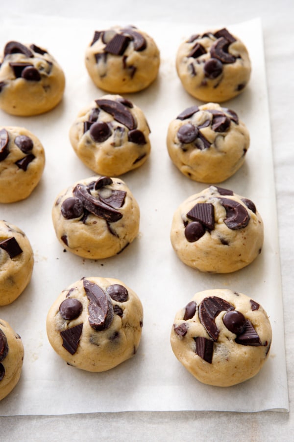Balls of rolled and shaped Amaretto Chocolate Chip Cookie dough, with pieces of dark chocolate pressed into the top.