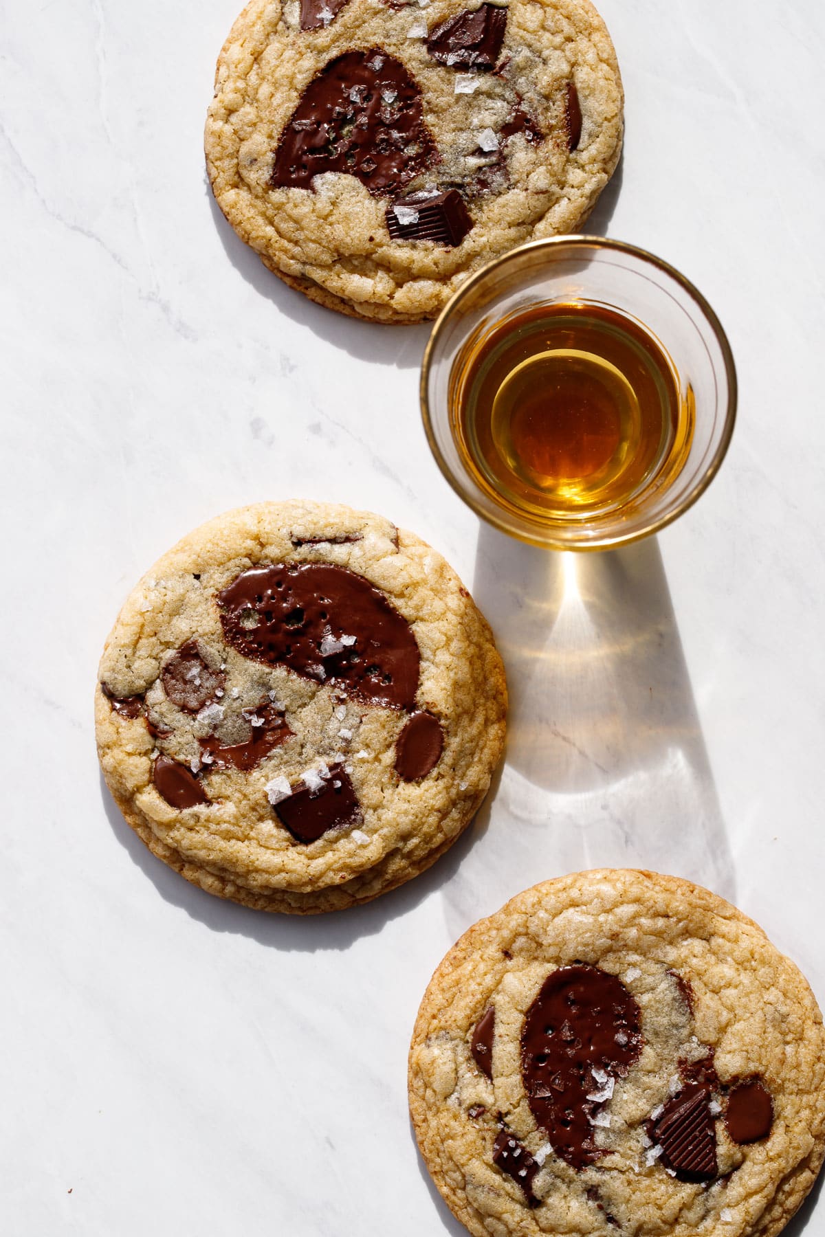 Three Amaretto Chocolate Chip Cookies on a marble background with a shot glass of amaretto liqueur.