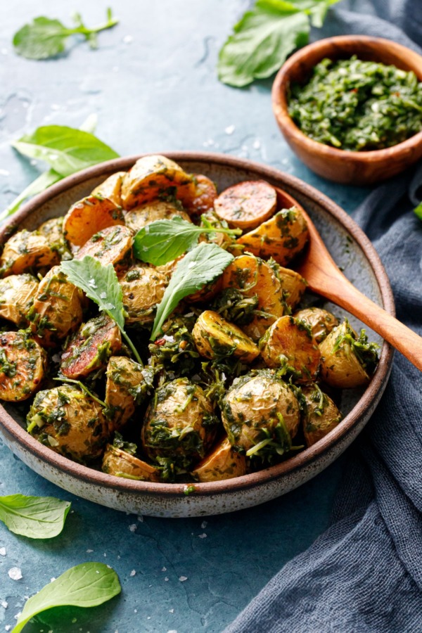 Shallow bowl filled with roasted potatoes tossed with arugula chimichurri, small baby arugula leaves scattered on top