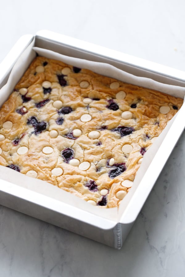 Square aluminum baking pan with freshly baked Blueberry White Chocolate Blondies, on marble background.
