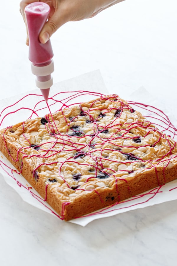 Drizzling a hot pink blueberry glaze in artful swirls on top of Blueberry White Chocolate Blondies.