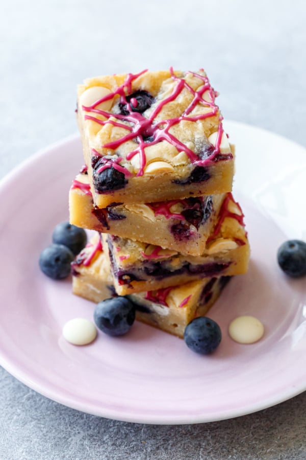 Stack of 4 Blueberry White Chocolate Blondies on a purple plate, with swirls of hot pink blueberry glaze.