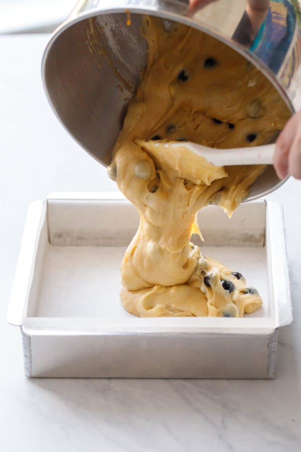 Pouring Blueberry White Chocolate Blondie batter into a parchment-lined square baking pan.