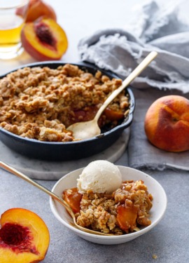 Skillet Bourbon Peach Crisp with fresh peaches on the side and a shot glass of bourbon.