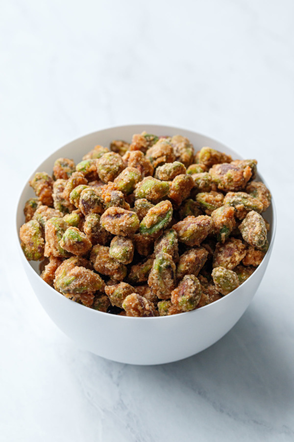 A white porcelain bowl full of spiced candied pistachios
