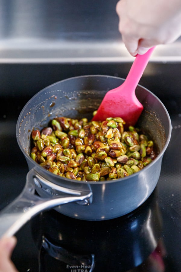Stirring the pistachios into the sugar syrup in a small saucepan on the stove.