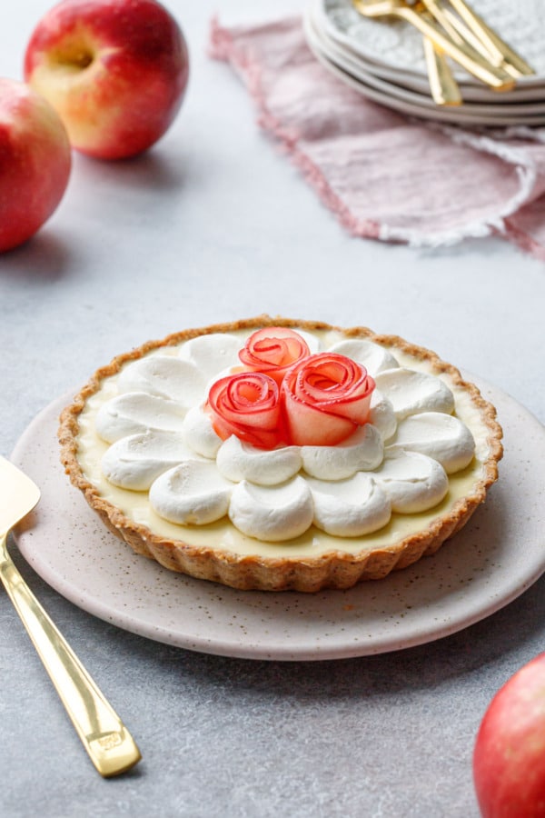 Caramel Apple Mousse Tart with Apple roses on a flat ceramic plate, whole red apples in the background.