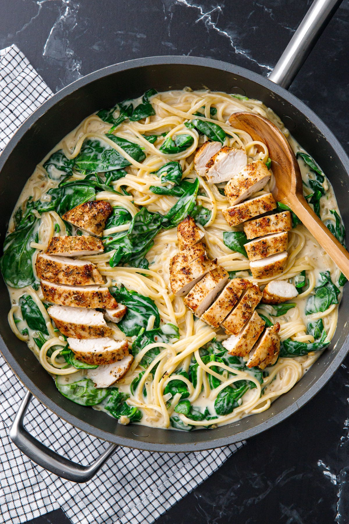 Overhead, nonstick skillet with Creamy Chicken Florentine linguine with wilted spinach and browned chicken tenders cut into strips.