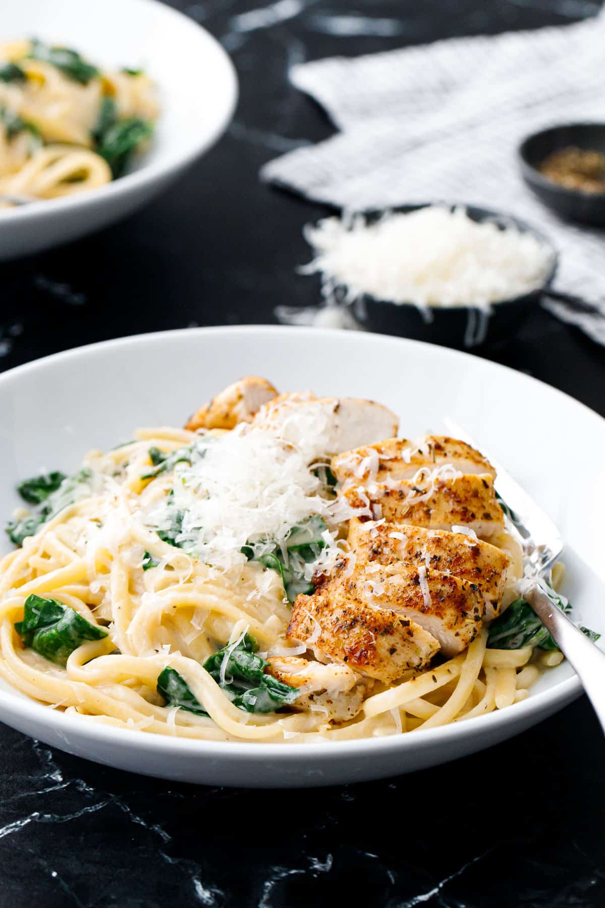 Closeup, bowl of Creamy Chicken Florentine Pasta with a browned chicken tender cut into pieces and topped with finely shaved parmesan cheese.
