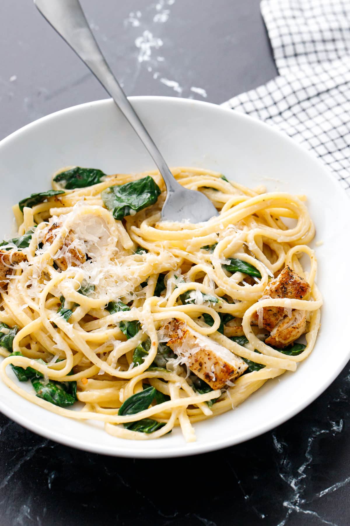 Bowl with Creamy Chicken Florentine Pasta topped with parmesan cheese, with a silver fork digging in.