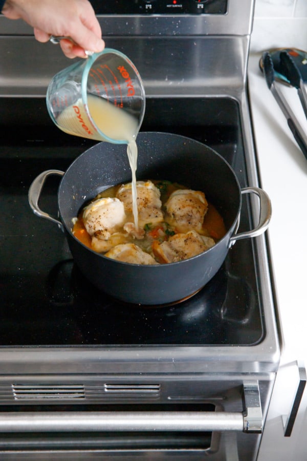 Pouring chicken stock into saucepan with chicken thighs and vegetables.