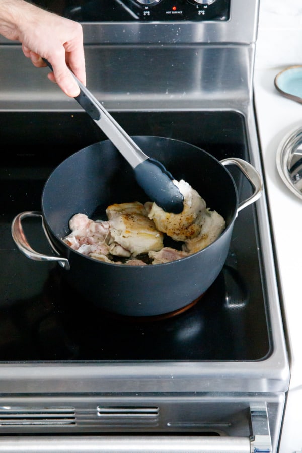 Browning boneless chicken thighs in a saucepan, flipping with tongs when one side is browned.