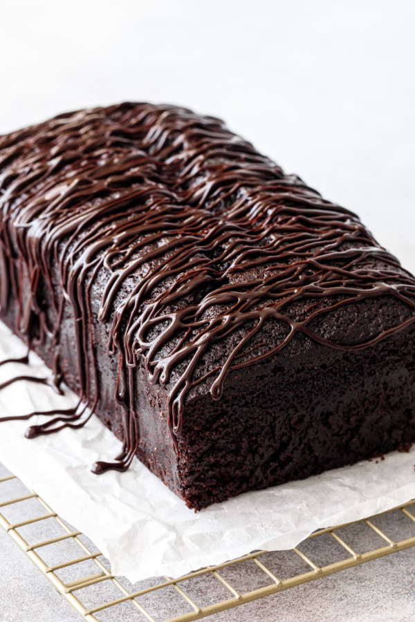 Closeup, shiny chocolate drizzled glaze on a dark chocolate olive oil loaf cake.