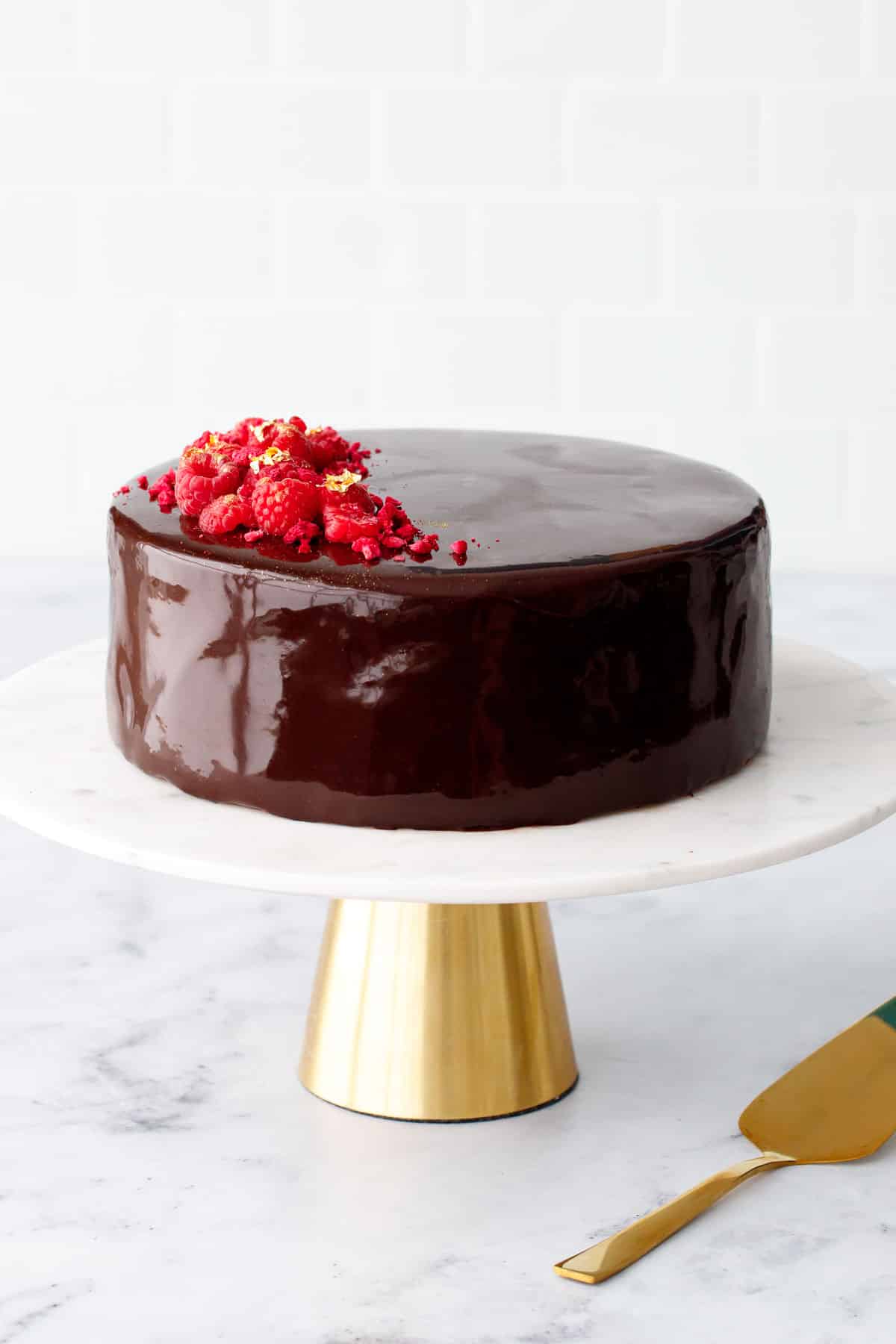 Chocolate Raspberry Mousse Cake with a super shiny chocolate mirror glaze and decorated with fresh and freeze dried raspberries and gold leaf accents.