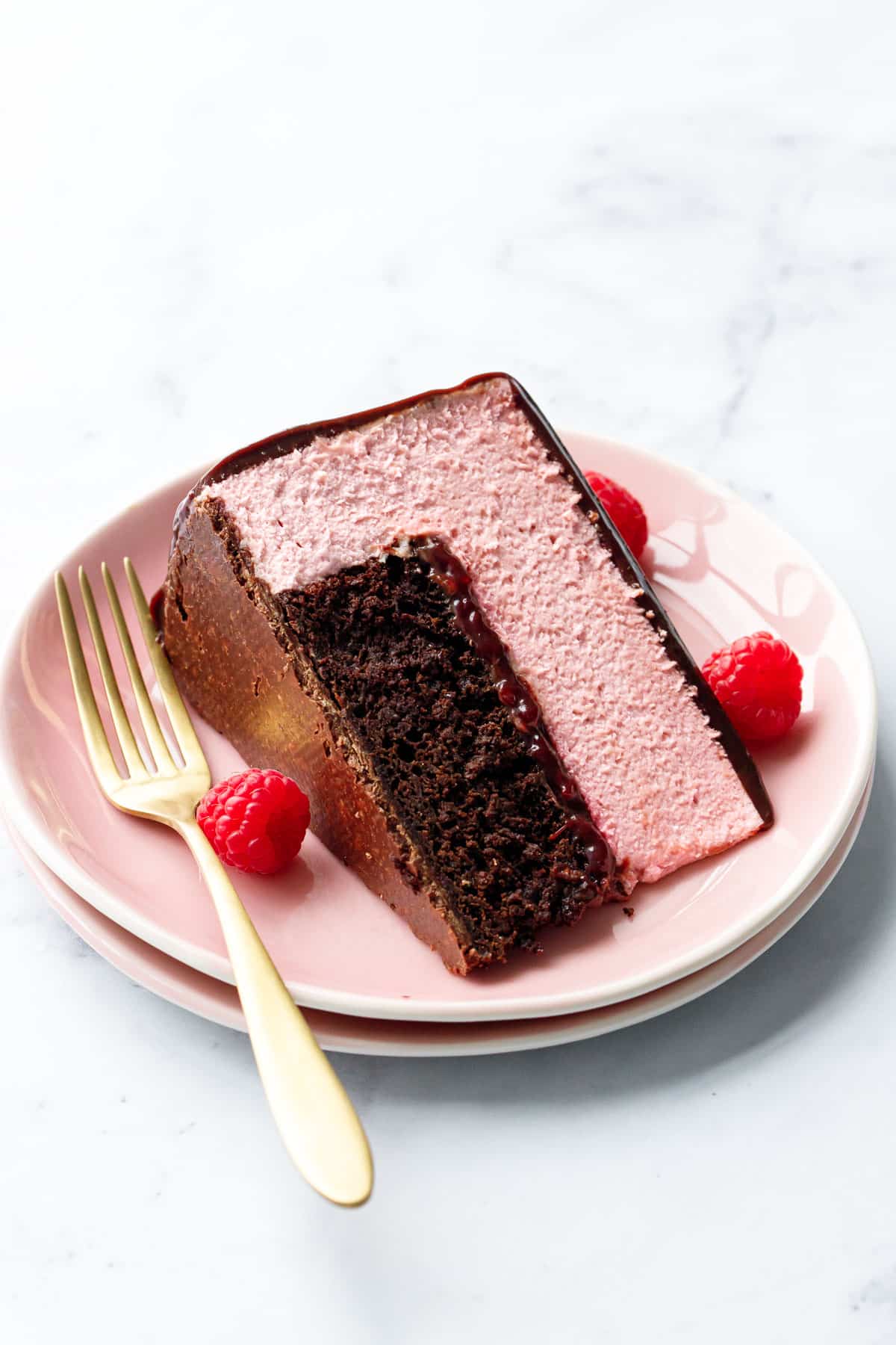 Slice of Chocolate Raspberry Mousse Cake laying on its side on a pink plate with raspberries and gold fork.