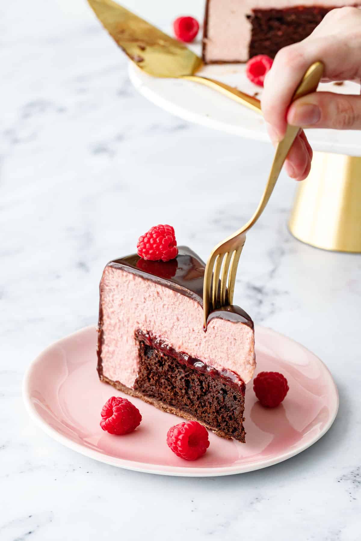 Slice of Chocolate Raspberry Mousse Cake with a gold fork cutting off a bite, gold and marble cake stand in the background.