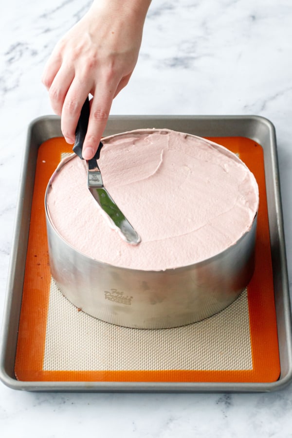 Small offset spatula spreading the top of the pink raspberry mousse into an even layer.