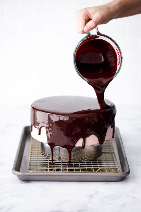 Glazing a Chocolate Raspberry Mousse Cake with dark chocolate mirror glaze, drips of glaze coming down and covering the top and sides.