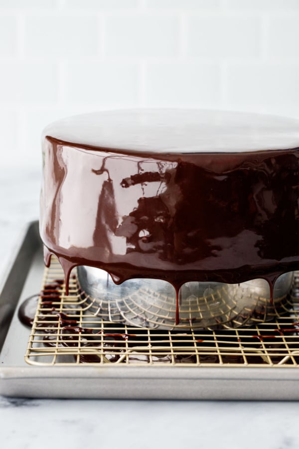 Fully glazed mousse cake with extra shiny finish, visible drips coming off the sides of the cake onto the baking sheet below.