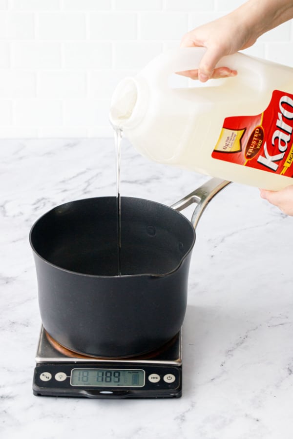 Pouring Karo syrup corn syrup into saucepan sitting on a kitchen scale.