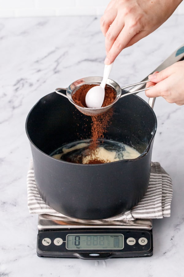 Sifting cocoa powder through a small mesh sieve into the saucepan with the sugar mixture.
