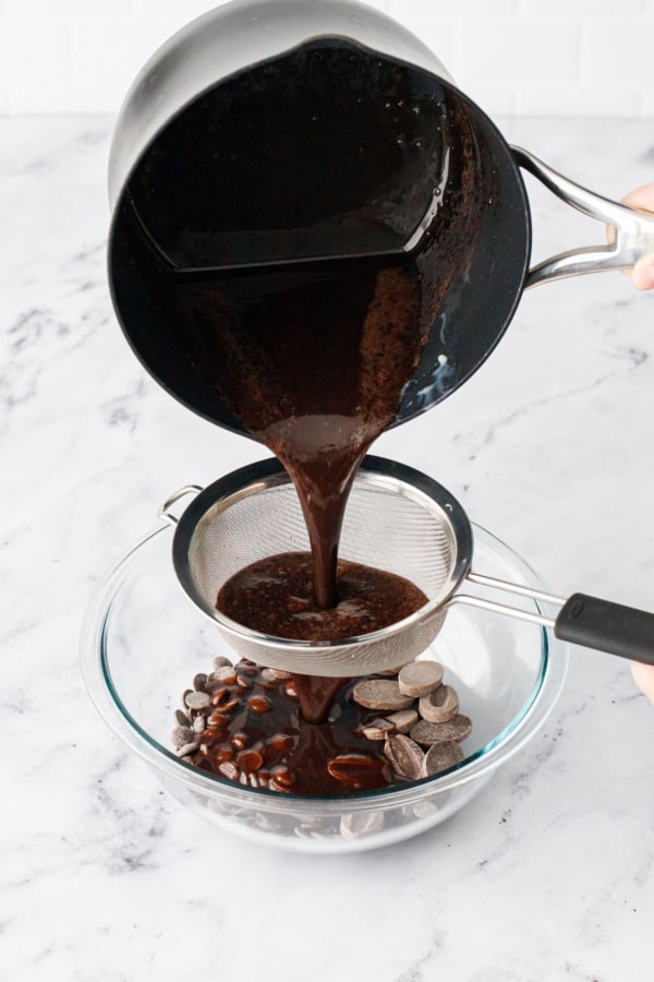 Pouring the liquid glaze through a fine mesh sieve into a bowl with dark chocolate.