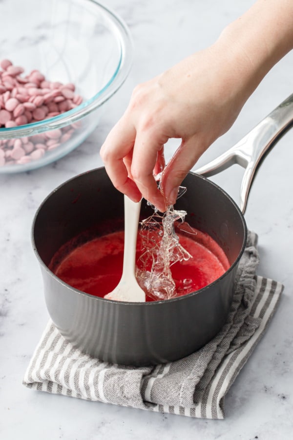 Adding softened leaf gelatin to a small saucepan with warm raspberry puree.