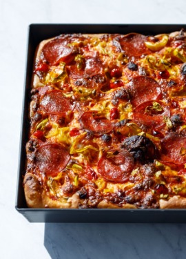 Detroit-style pan pizza styled in harsh light topped with pepperoni and pickled peppers.