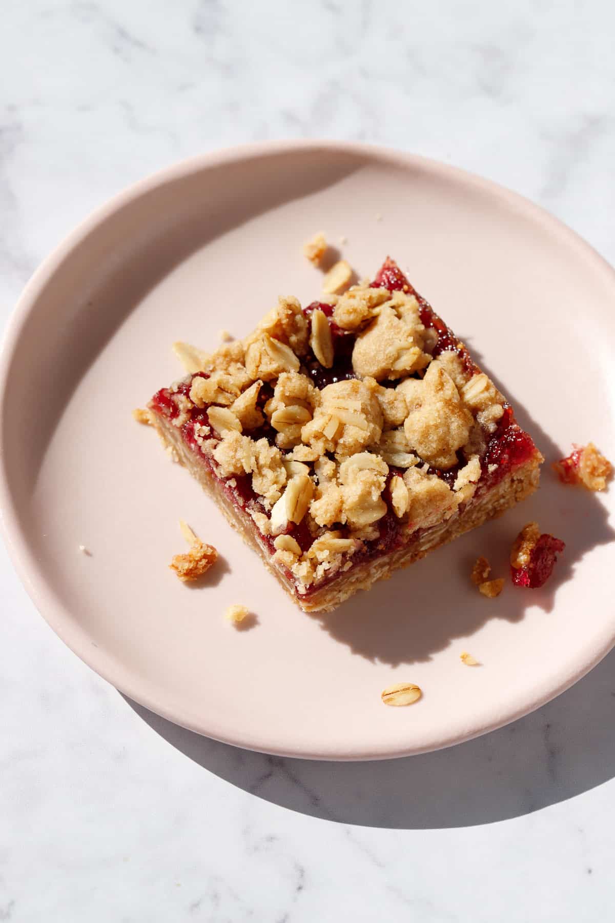 Single square Fig, Apple & Vanilla Crumb Bar on a pink plate with crumbs scattered around.