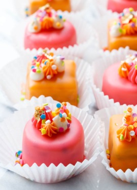 Rows of pink and orange "Funfetti Fours" with buttercream decorations and rainbow sprinkles
