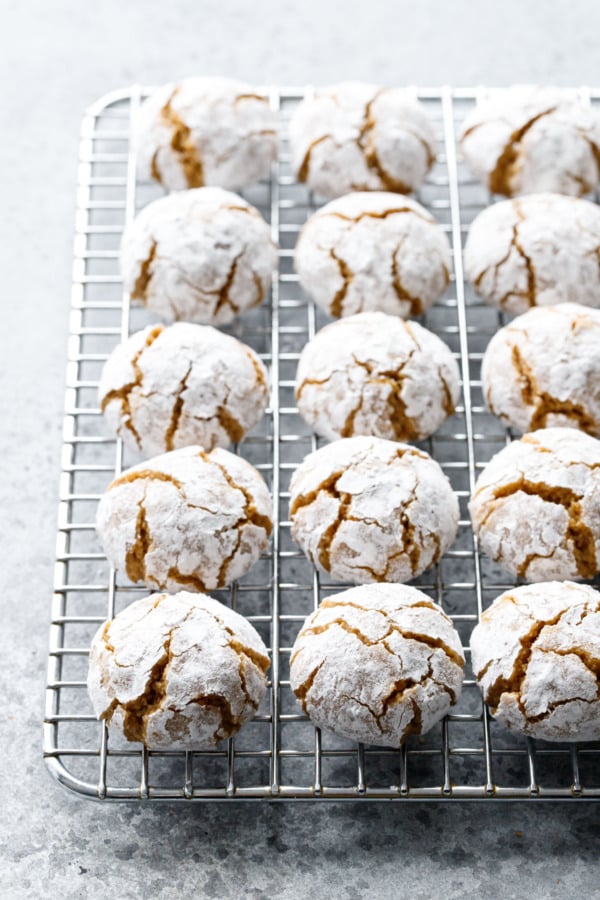 Wire rack with neat rows of crinkled Gingerbread Amaretti Cookies, coated in powdered sugar with cracks of cookie showing through.