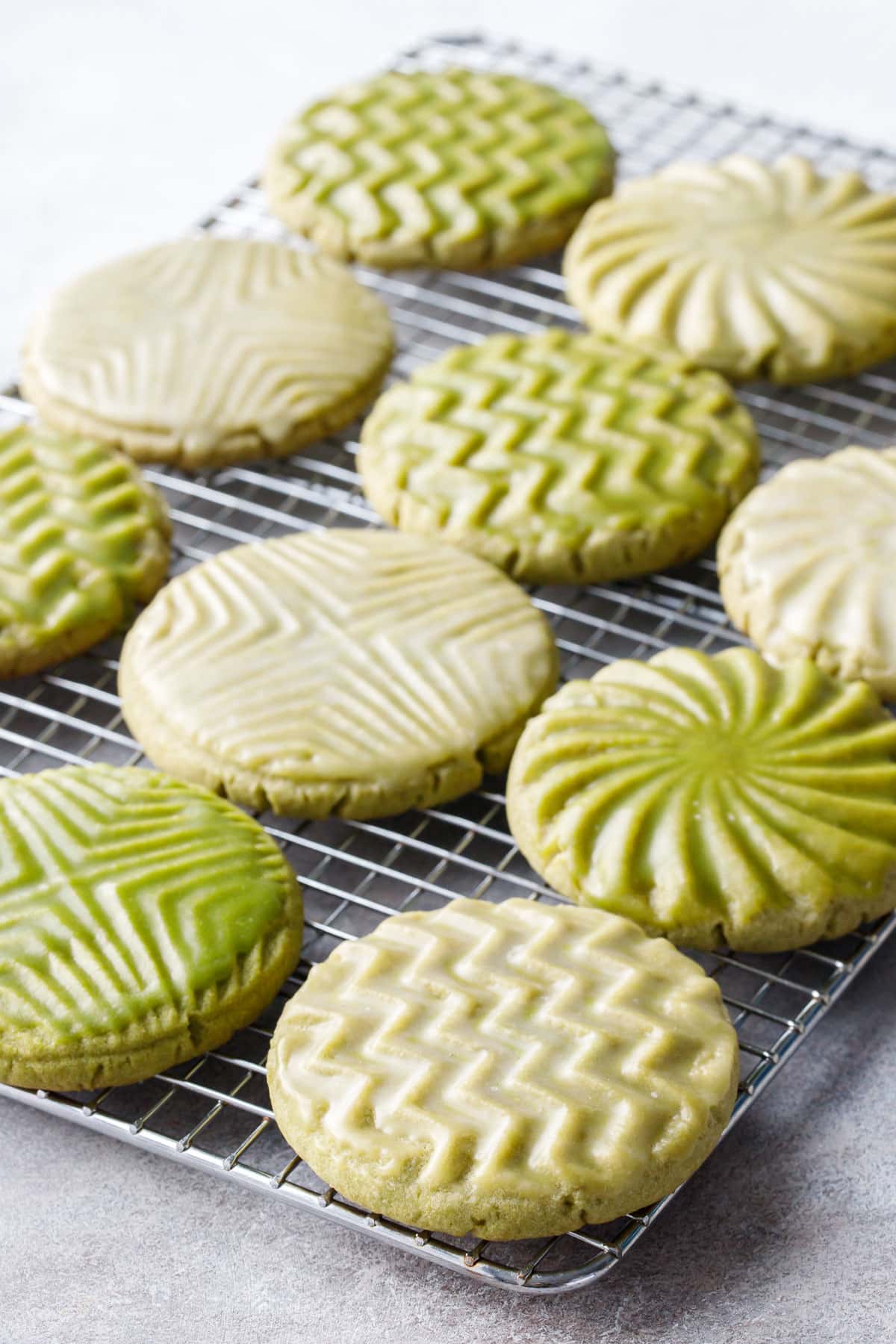 Wire rack with rows of Glazed Matcha Sugar Cookies with geometric designs and alternating white and green glazes.