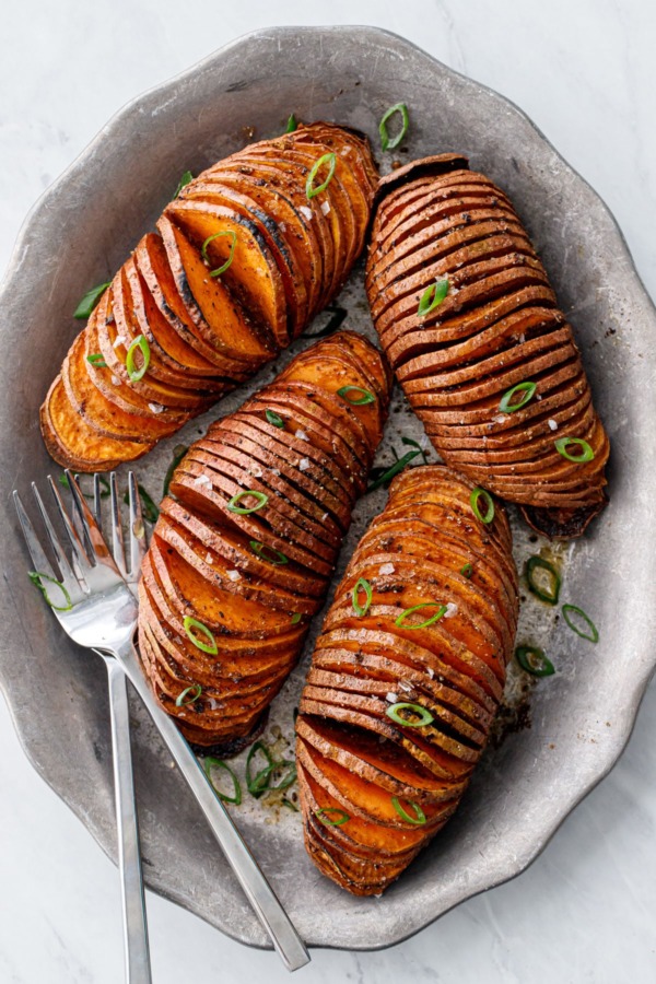 Overhead view of four Hasselback Sweet Potatoes arranged on a metal plate with forks