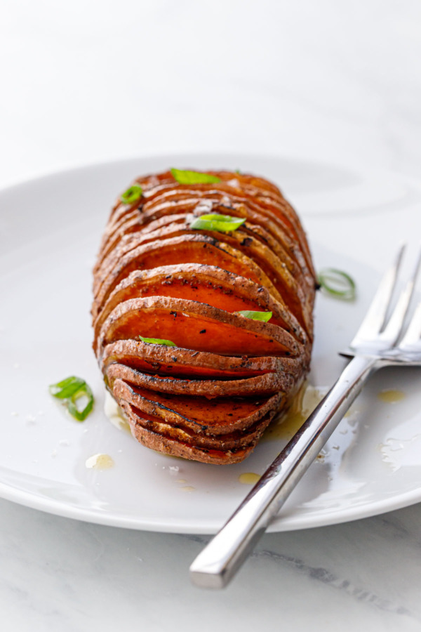 Spiced Hasselback Sweet Potato on a white plate with a fork