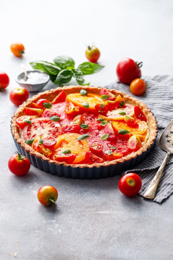 Heirloom tomato and goat cheese tart on a gray background surrounded by heirloom tomatoes