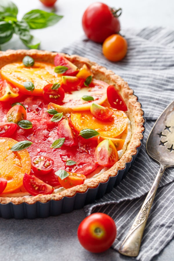 Goat Cheese & Heirloom Tomato Tart with a gray striped linen and vintage silver pie server