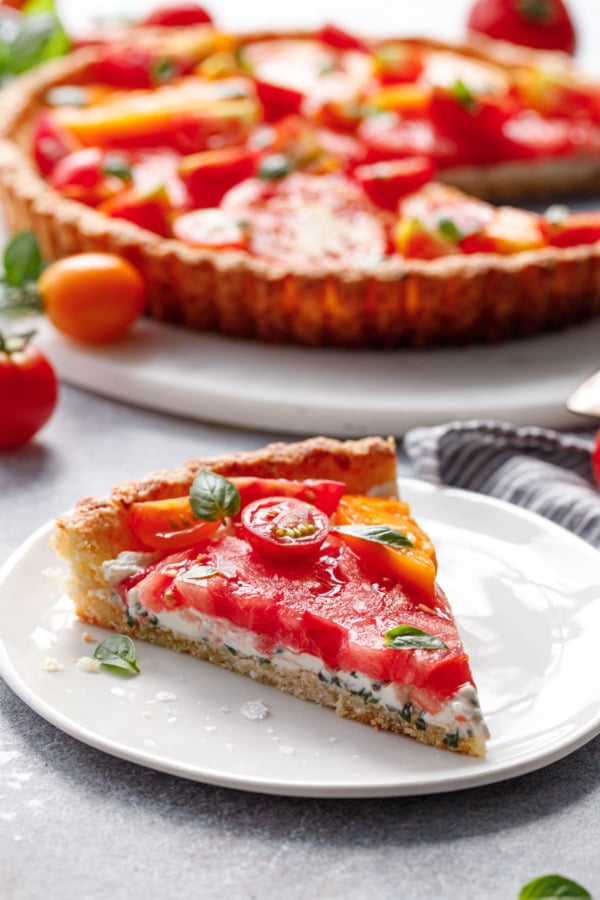 Slice of heirloom tomato tart showing the layers of tomato, goat cheese, and parmesan crust.