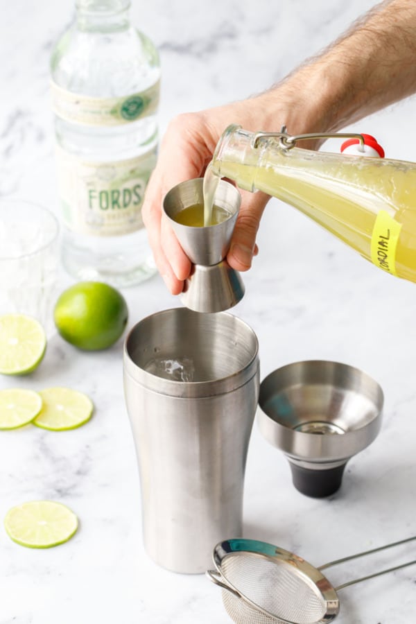Measuring Homemade Lime Cordial into a jigger, then pour into a cocktail shaker with gin and ice.