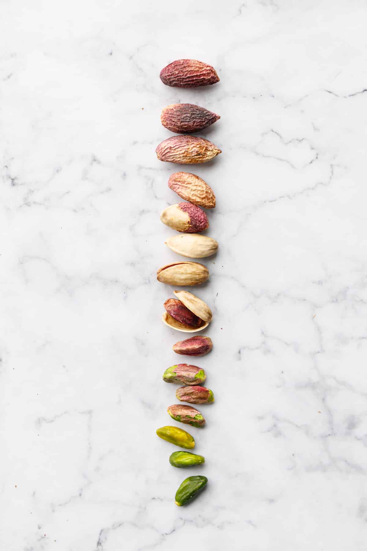 Gradient of pistachios, with whole nuts still in the outer skins at the top, down to the fully peeled and blanched bright green nuts at the bottom.