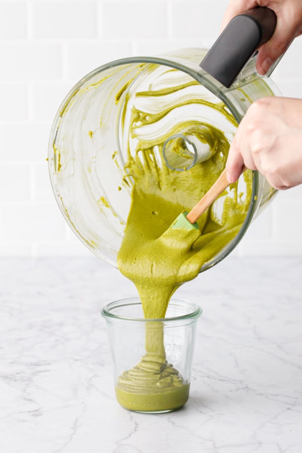 Scraping the smooth and creamy Homemade Pistachio Butter out of the food processor and into a glass jar.