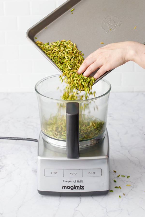 Pouring toasted slivered pistachios into a food processor.