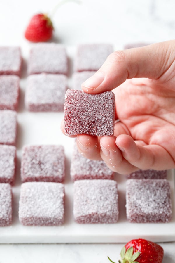 Squeezing a square piece of Homemade Sour Strawberry Gummy candy to show texture (frame 1).