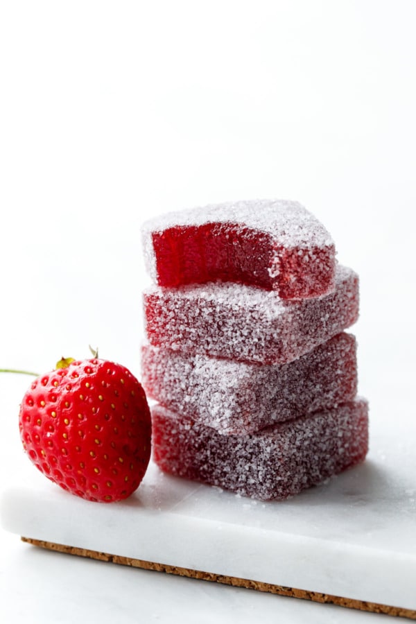 Stack of 4 Homemade Sour Strawberry Gummies, one with a bite out of it and a single strawberry on the side.