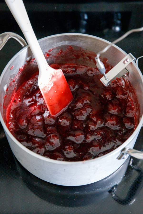 Saucepan with bubbling strawberry mixture and spatula, with a probe thermometer attached to the side.