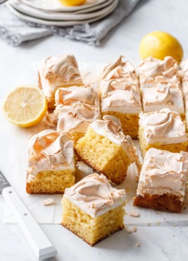 Cut squares of Lemon Meringue Butter Cake on a marble background with white knife and stack of plates in the background.