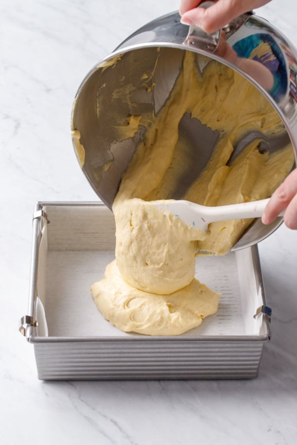 Pouring the thick butter cake batter into a parchment-lined square baking pan.
