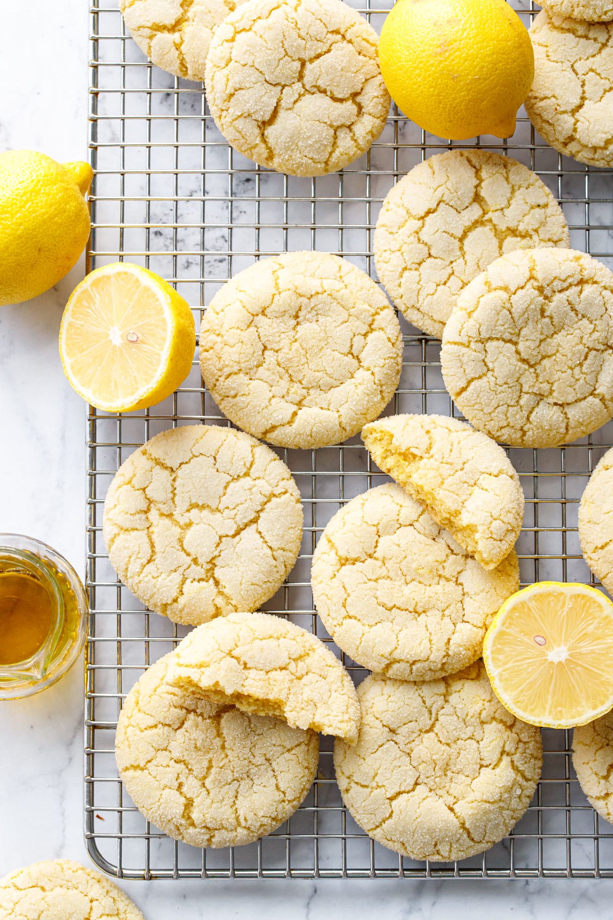 Overhead, Lemon Olive Oil Sugar Cookies on a wire baking rack, haphazardly arranged with whole and cut lemons and a dish of olive oil.