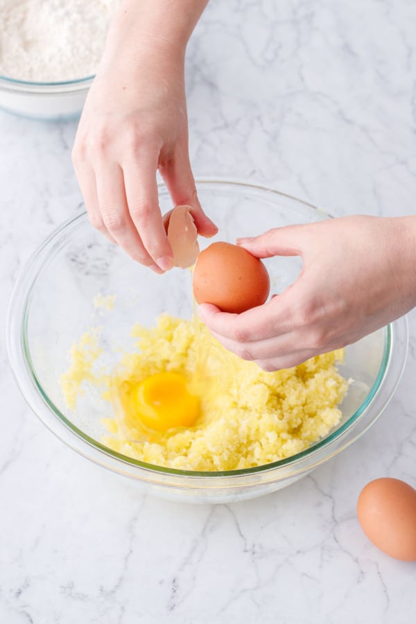 Cracking an egg into a glass mixing bowl, another egg sitting beside the bowl.