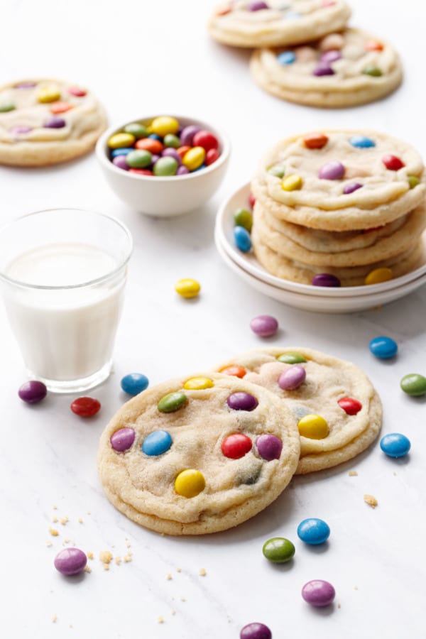 M&M Sugar Cookies on a marble background, with glass of milk, bowl of candies, and plate of cookies in the background.