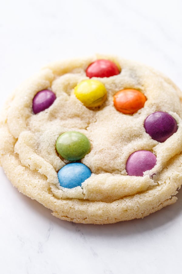 Extreme closeup to show the sugary coating and ruffled texture of an M&M Sugar Cookie, marble background.